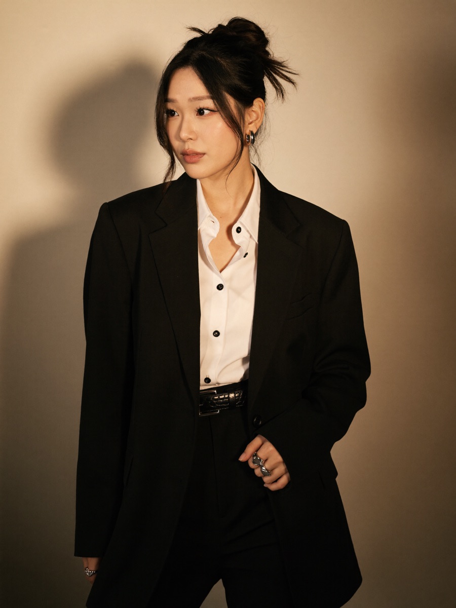 Black blazer and white shirt in warm golden side light, sleek updo, beige wall