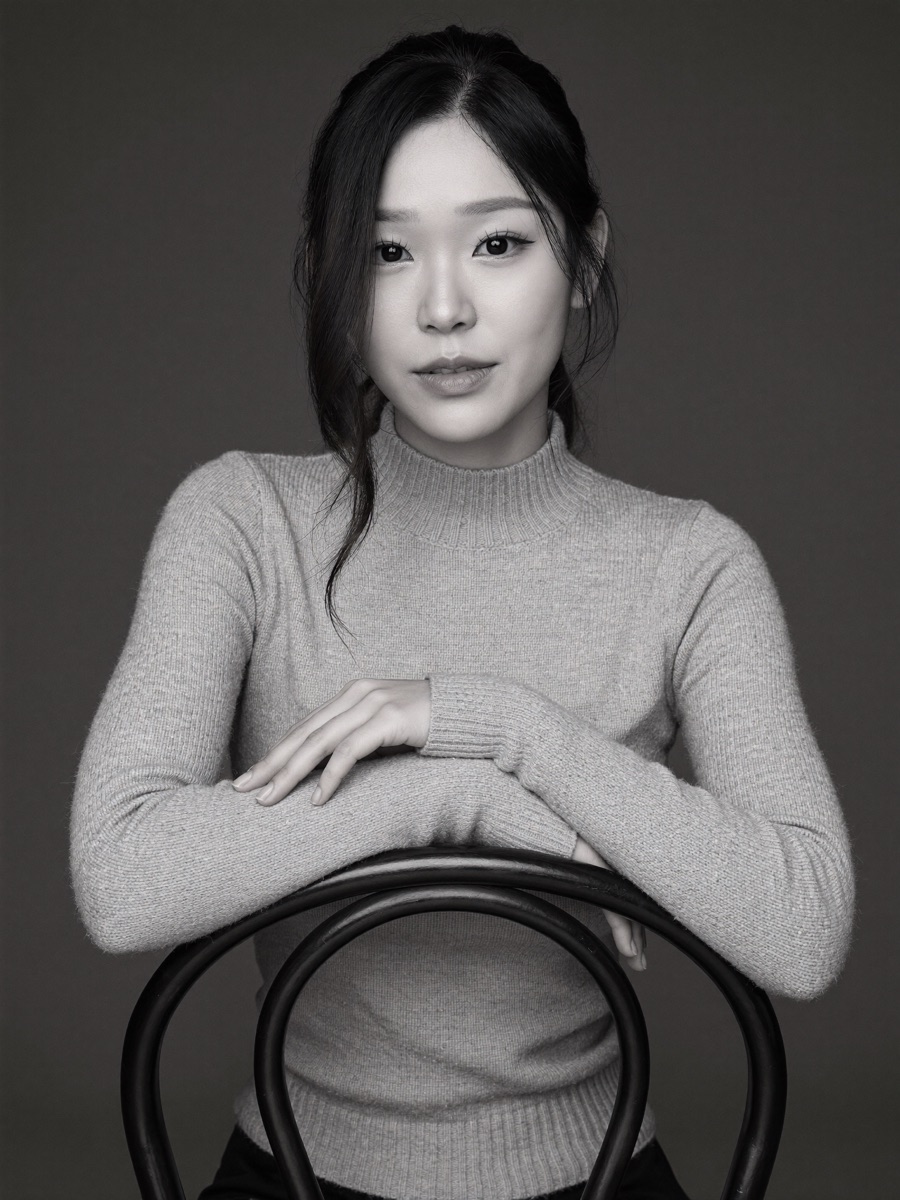 Seated backward on a metal chair in a ribbed turtleneck, black and white