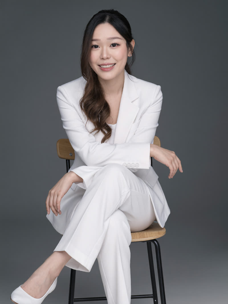 AI LinkedIn headshot: white tailored pantsuit, seated on a wooden chair against a dark grey studio backdrop