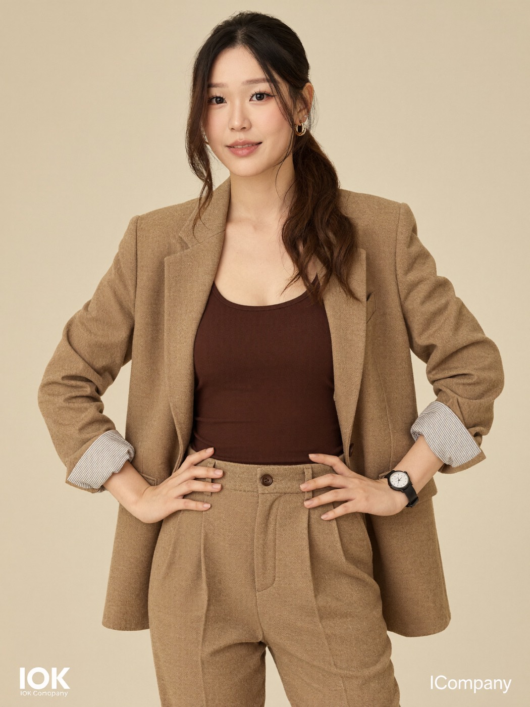 Camel wool suit with hands on hips on a beige backdrop