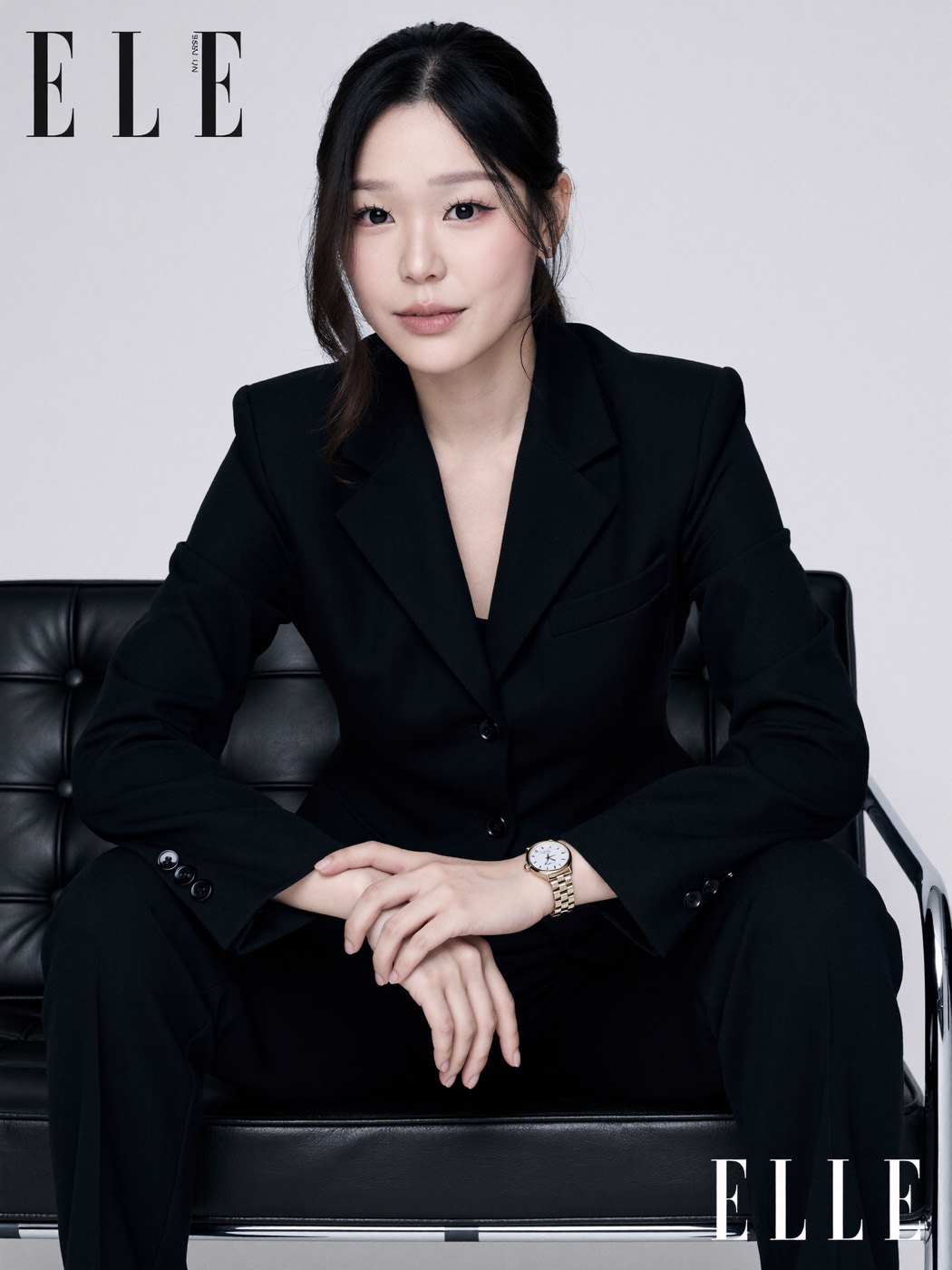 Black suit seated on a black leather and chrome bench, white studio